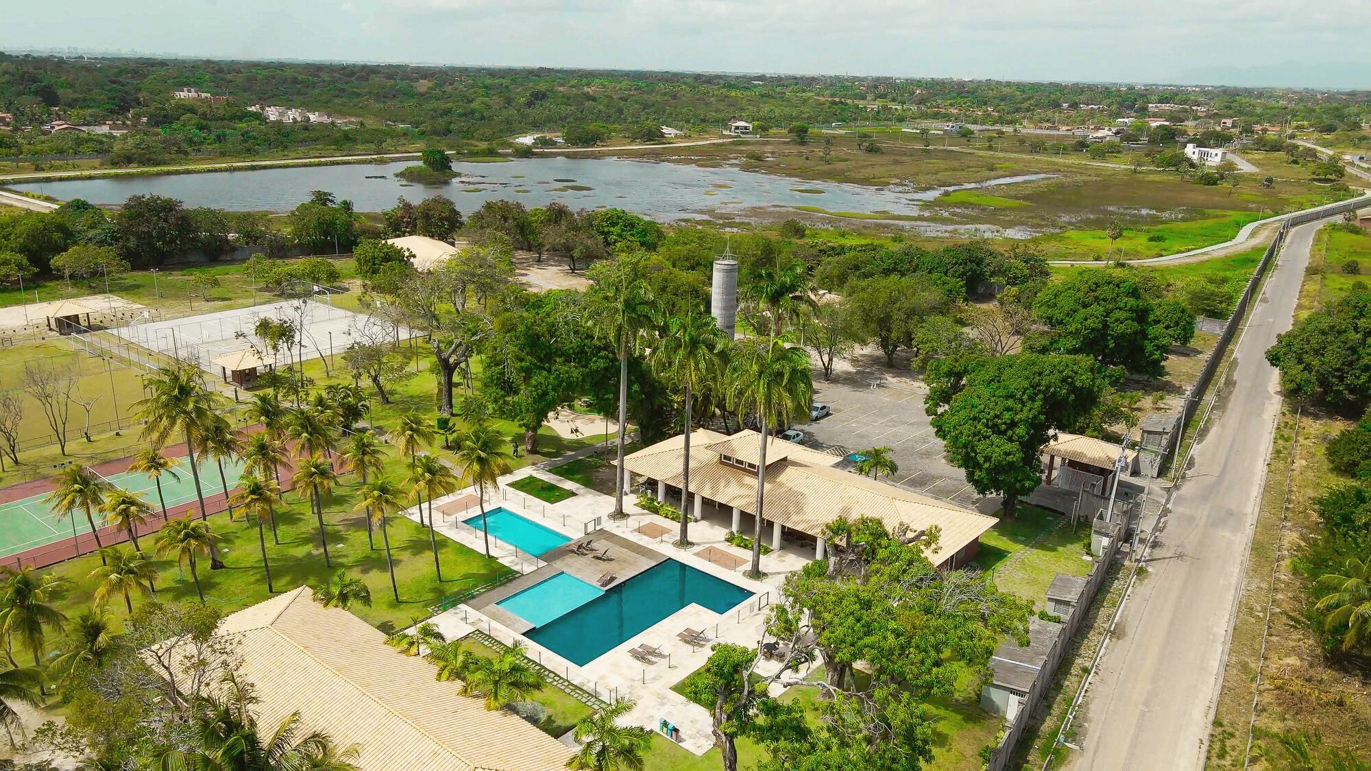 Vista aérea do Home Club com piscinas, coqueiros e o lago ao fundo