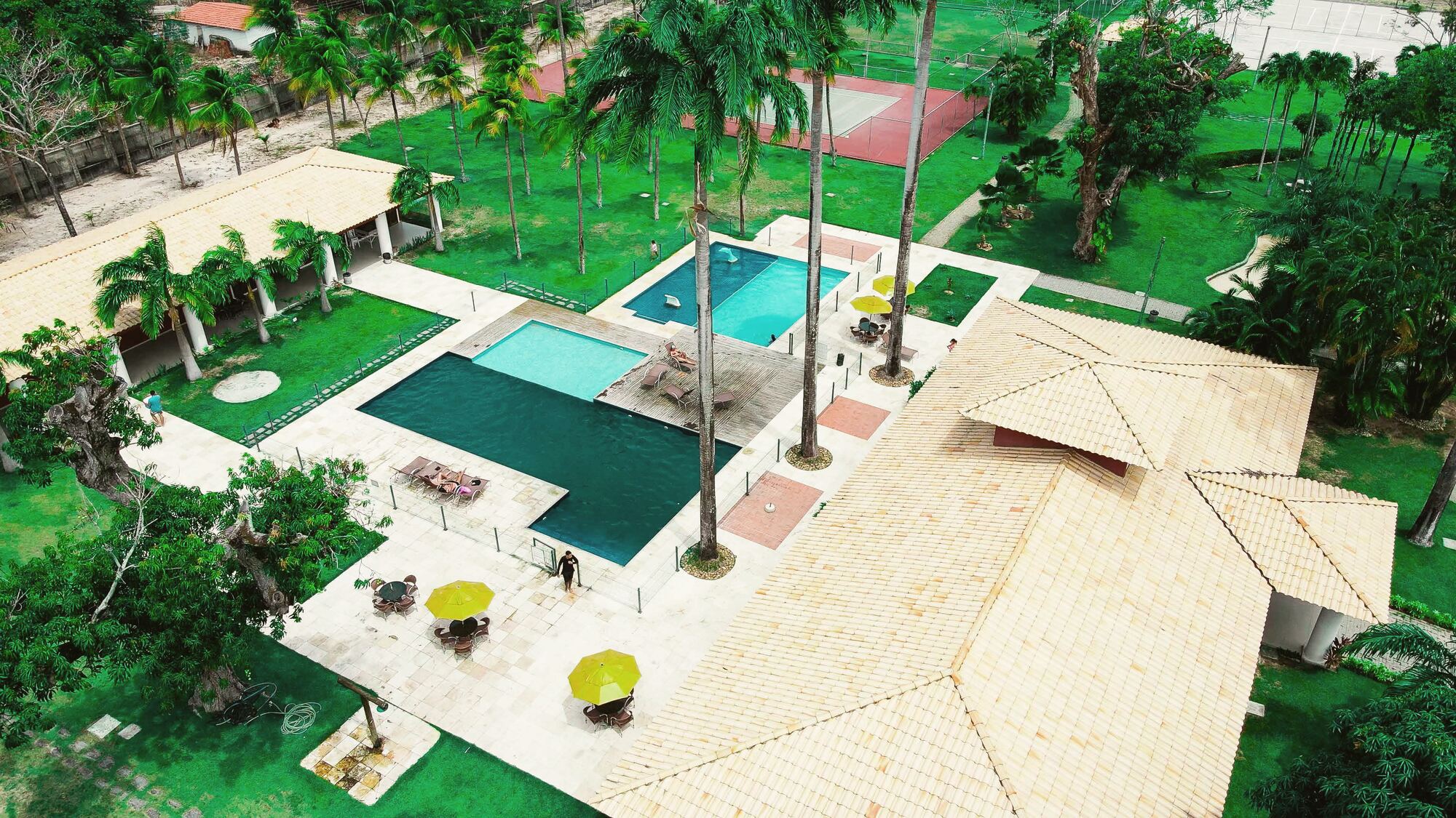 Piscinas do Home Club vistas de cima, com coqueiros e guarda-sóis